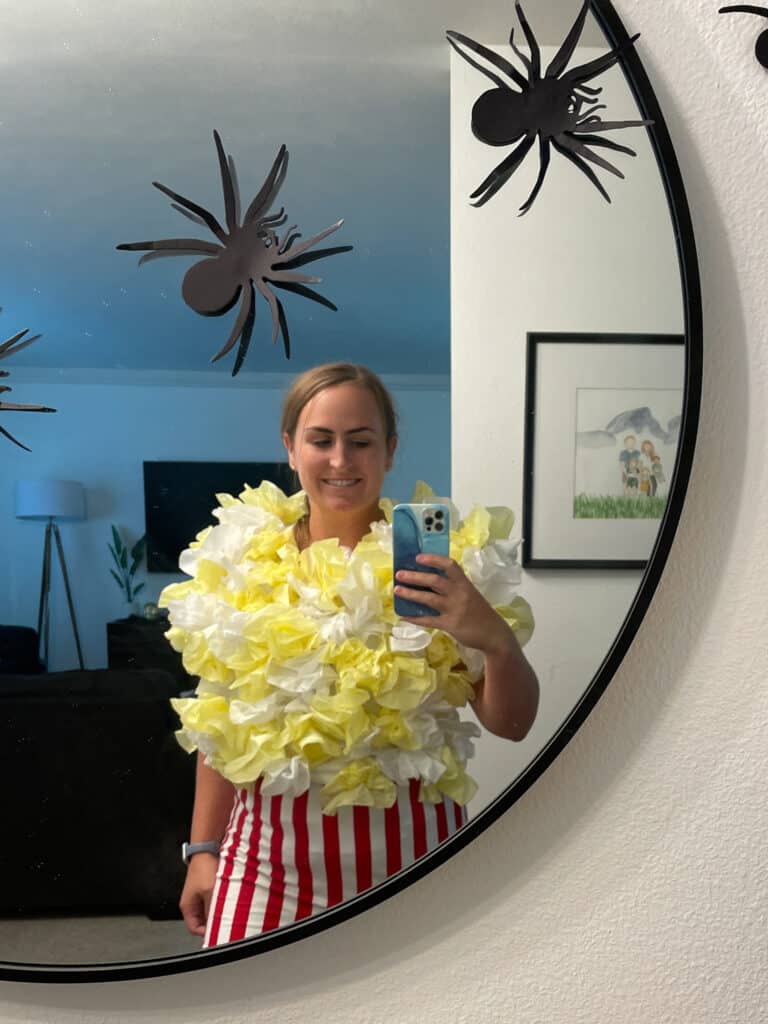 Woman standing in a mirror trying on a handmade popcorn costume to check for fit.