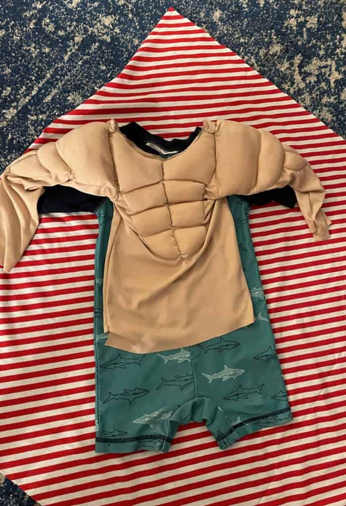 Red and white knit fabric laid out flat with swimsuit and muscle man shirt laid on top to create the jumper pattern