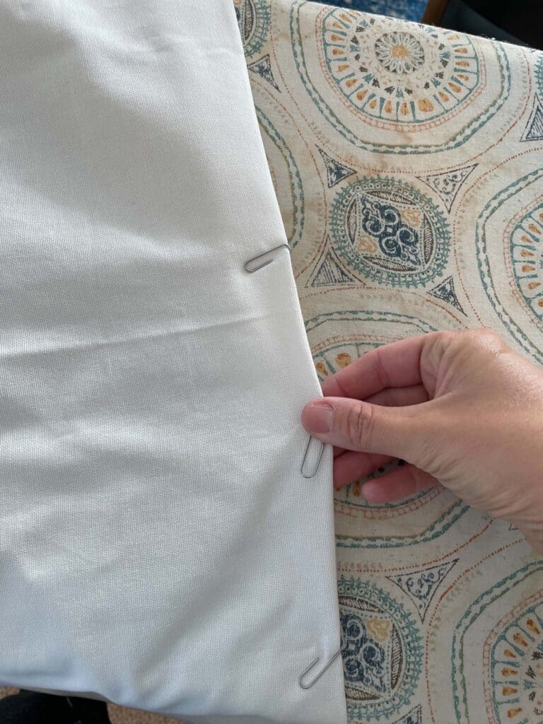 Hand holding the bottom edge of a curtain panel demonstrating how to remove a paperclip from the bottom of the panel