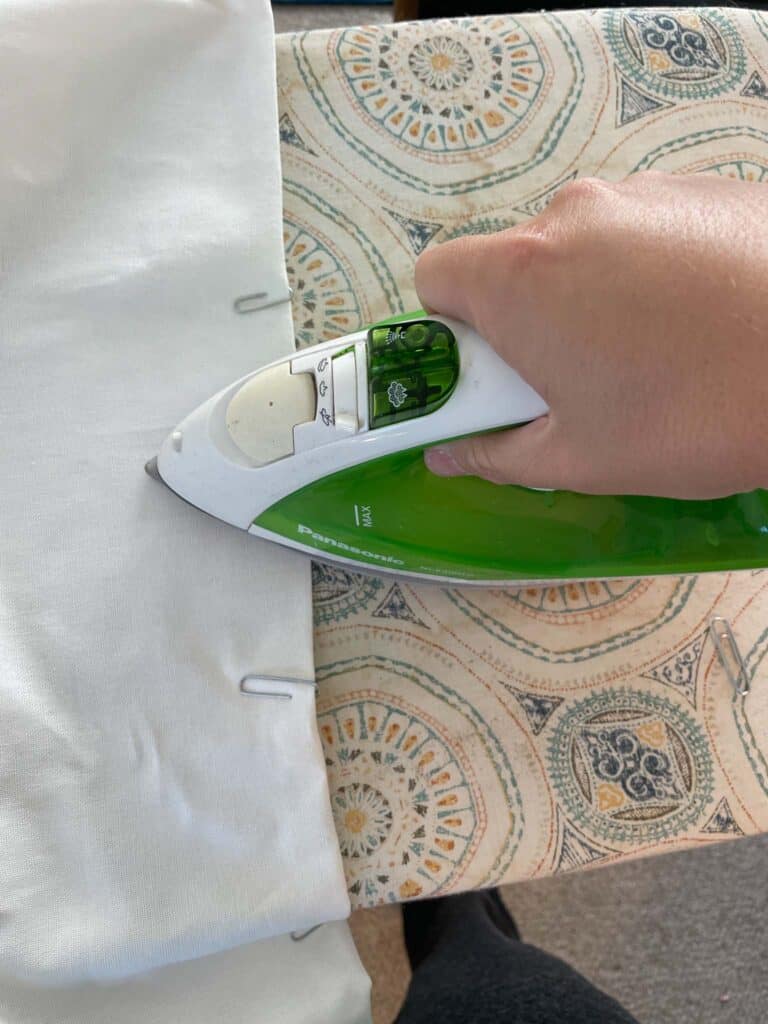 Curtain panel placed on ironing board and hem held in place with paper clips