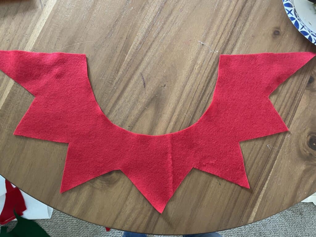 Red felt cut into a collar for elf costume laying on a wooden table.